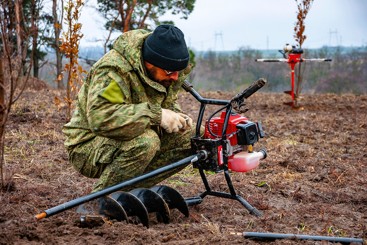 A forester crouches down to prepare an auger to plant seedlings